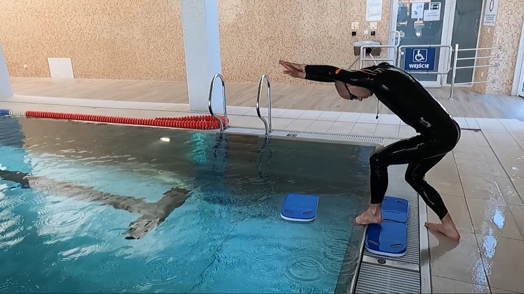 Skok do wody z pozycji stojącej przez przeszkodę (np. deskę na wodzie)